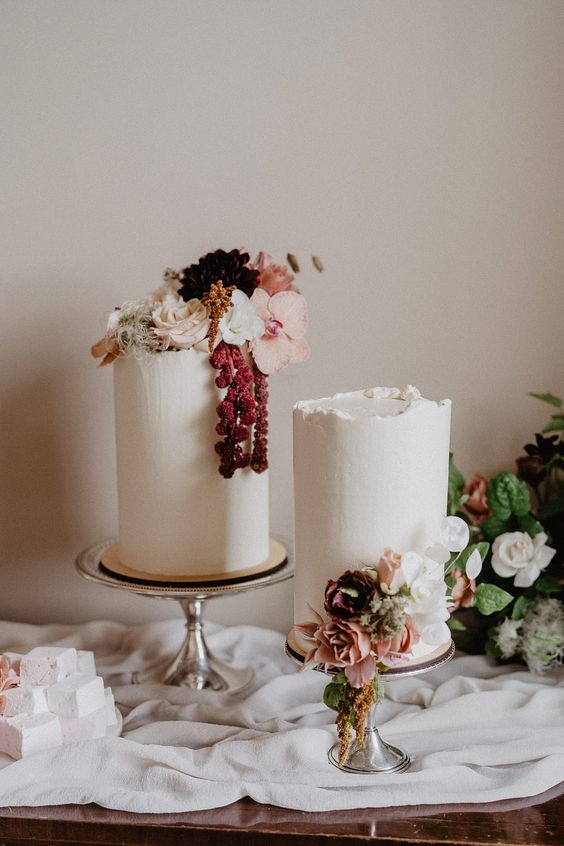 a duo of tall white wedding cakes decorated with pink, blush and white blooms and berries is chic for summer