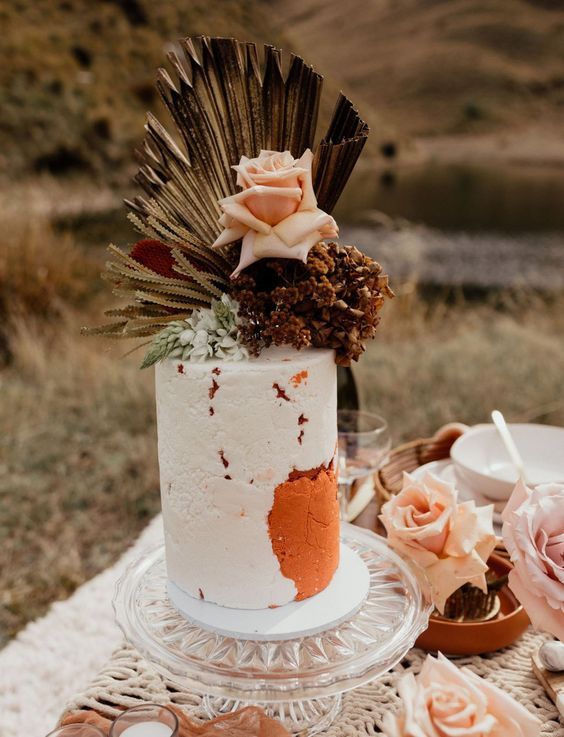 a fall boho wedding cake with an orange touch, fronds, dried and fresh blooms is a cool idea for a fall boho wedding