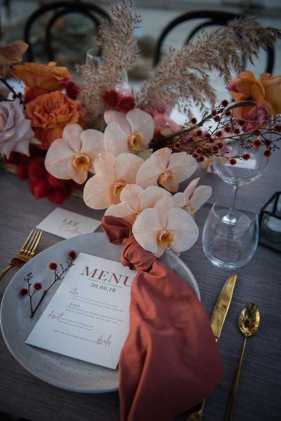 a fall wedding centerpiece of blush orchids, pale pink and rust roses, dried branches and burgundy fillers is wow