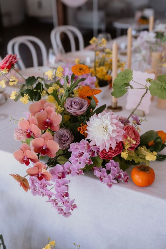 a fantastic bright wedding centerpiece of pink and coral orchids, lilac and pink roses, yellow and orange fillers