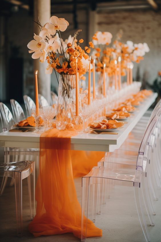 a fantastic tall wedding centerpiece of orange blooms and blush orchids paired with orange candles and a sheer table runner