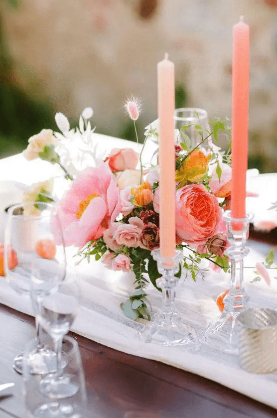 a gorgeous bright summer wedding centerpice of a pink peony, peony rose, small garden roses, bunny tails and a pink candle