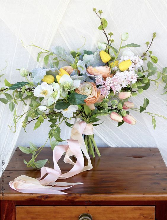 a gorgeous spring wedding bouquet of yellow and pink tulips, peachy ranunculus, white blooms, foliage, fillers and pink ribbon
