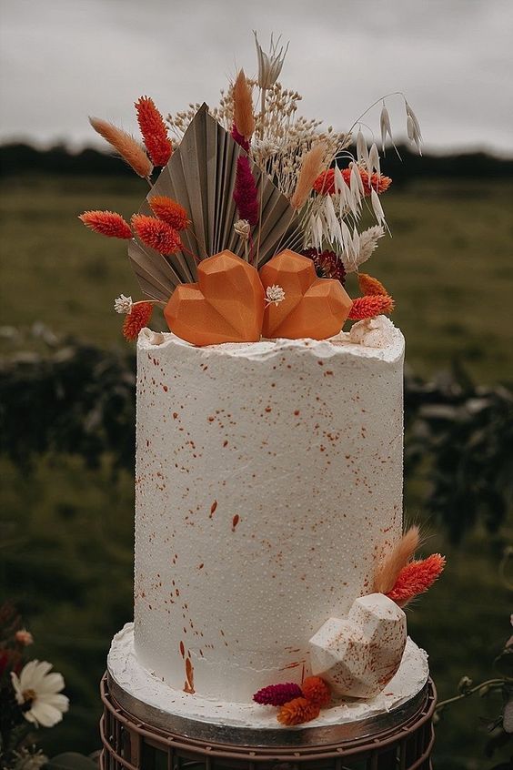 a gorgeous tall fall wedding cake with orange speckles, orange hearts, bunny tails, fronds and dried blooms