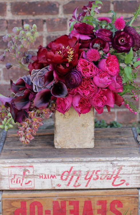 A jewel tone wedding centerpiece of burgundy peonies and roses, deep purple callas, hot pink peony roses and foliage