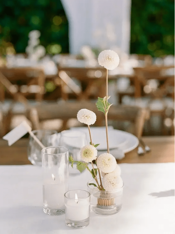 a lovely cluster wedding centerpiece of a couple of candles and white dahlias in a vase is a chic idea that you may realize yourself
