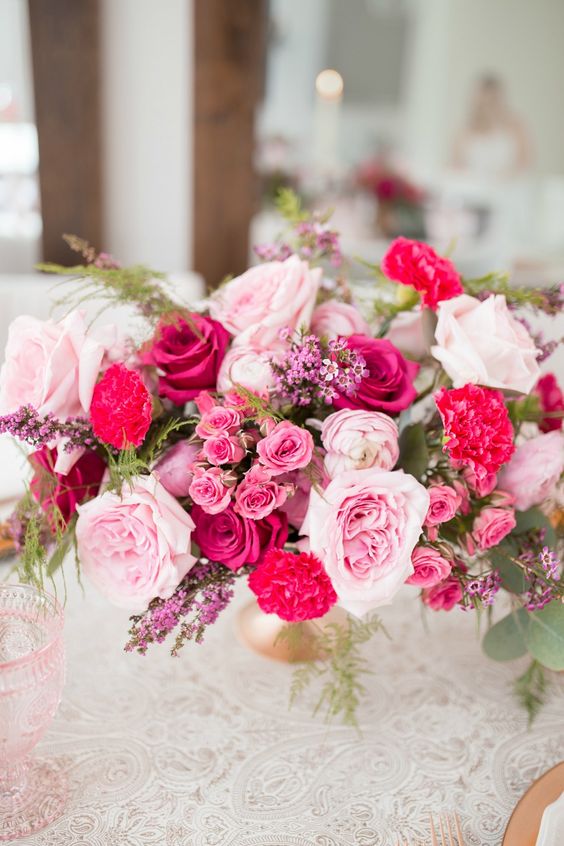 a lovely garden wedding centerpiece of light pink, pink roses, fuchsia roses and carnations and some pink fillers