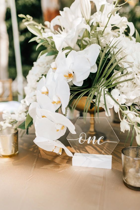a lovely modern tropical wedding centerpiece of white orchids, lilies and other white blooms and greenery is all cool