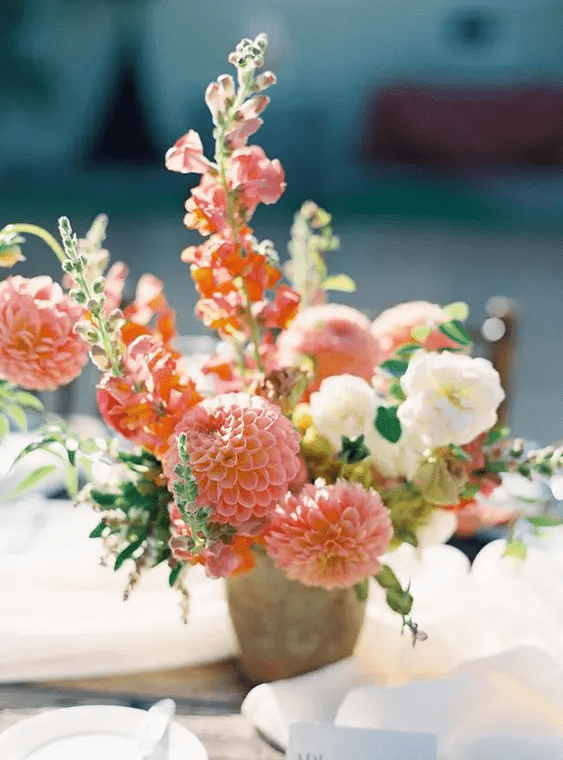 a lovely wedding centerpiece of pink dahlias, white roses and a bit of foliage for a coral summer wedding