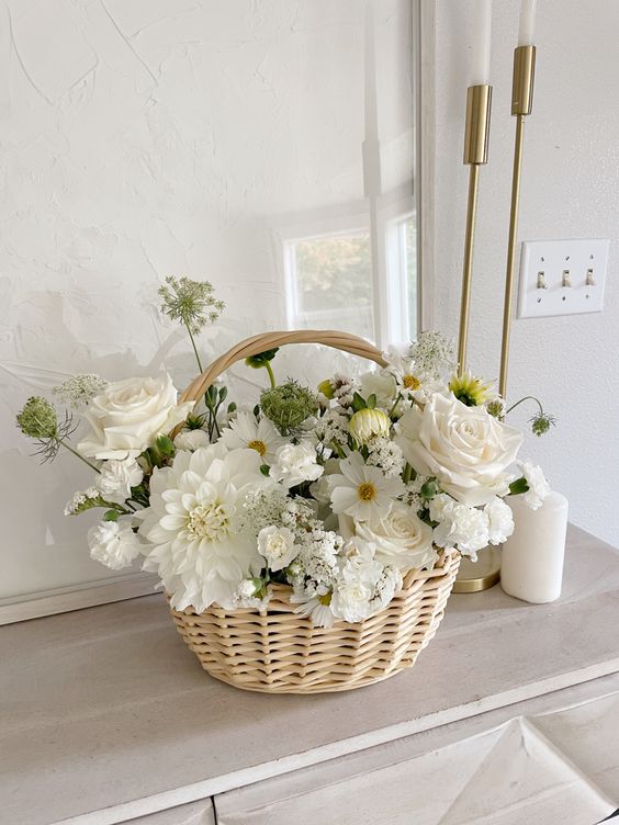 a lovely white wedding centerpiece of roses, dahlias, chamomiles and some fillers placed into a basket is super cool