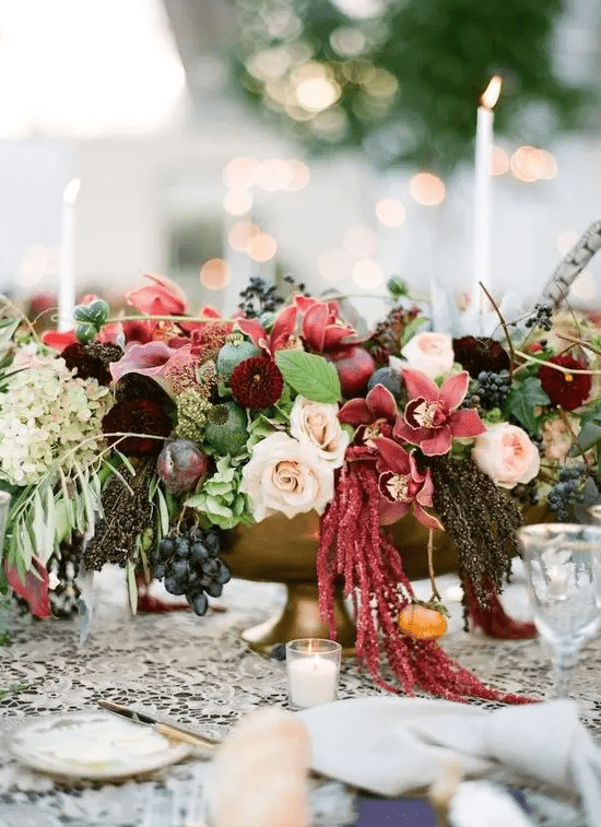 a lush and colorful fall wedding centerpiece of pink, mauve, burgundy, blush blooms, greenery and grapes plus a feather