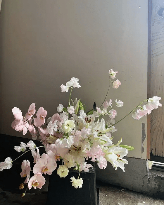 a lush neutral wedding centerpiece of white lilis, pink orchids, neutral blooms including sweet peas is a cool idea for spring or summer