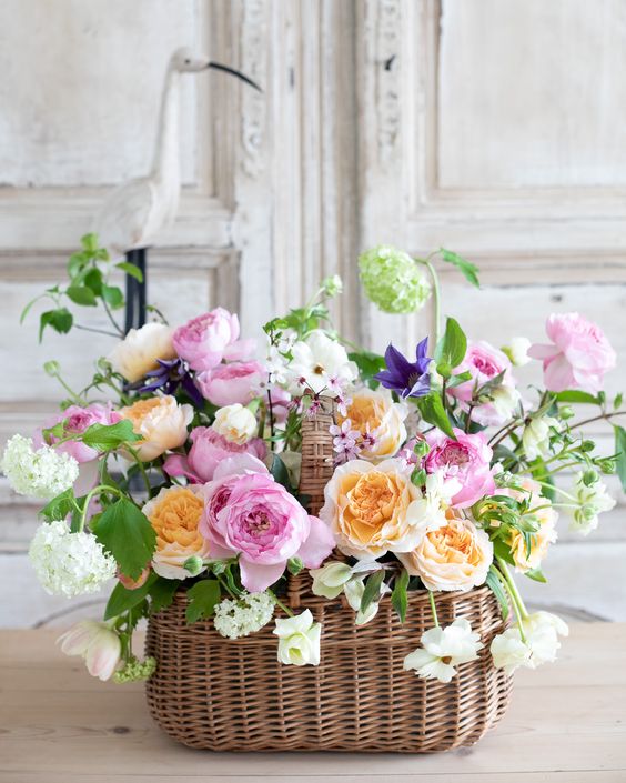 a lush wedding centerpiece of a basket with pink, peachy roses and peonies, greenery and white blooms for spring or summer