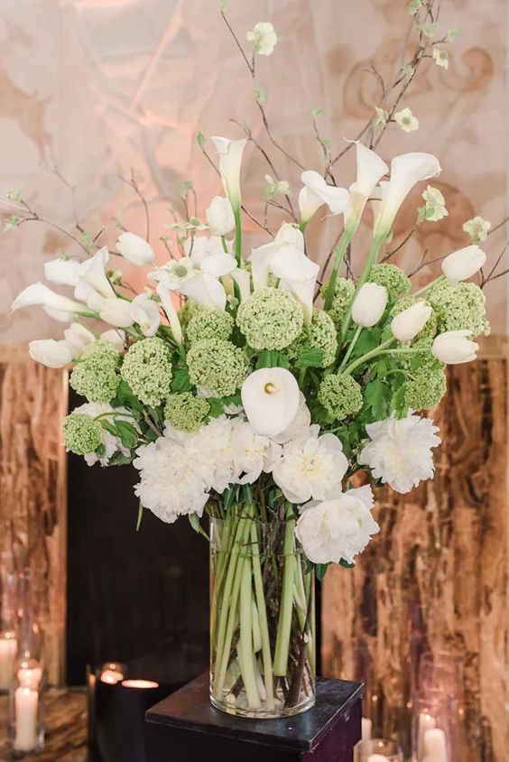 a lush white wedding centerpiece of greenery, white callas, carnations and blooming branches is a gorgeous decor idea