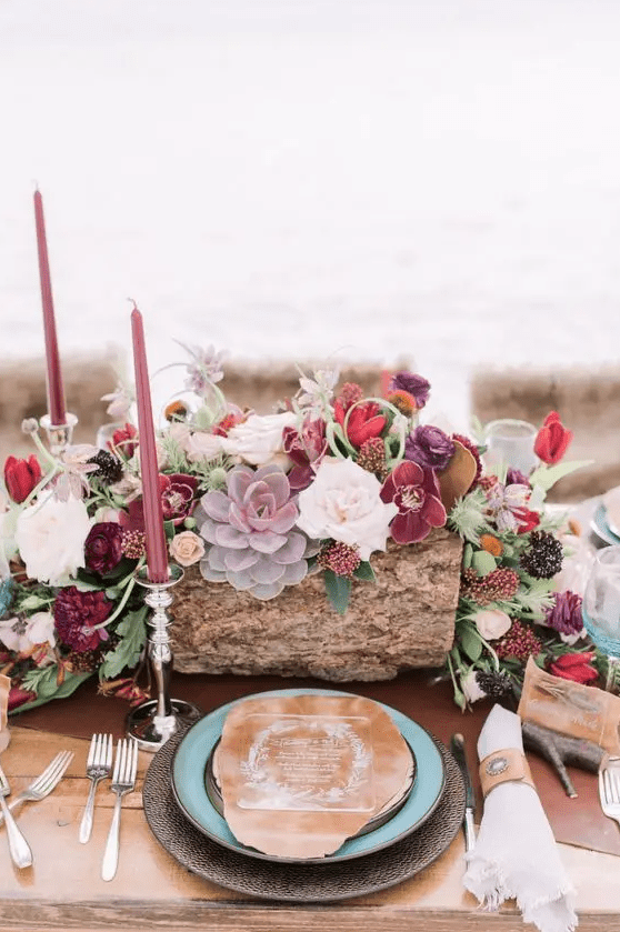a luxurious boho chic wedding centerpiece in the shades of burgundy, plum, pink, red plus colorful succulents