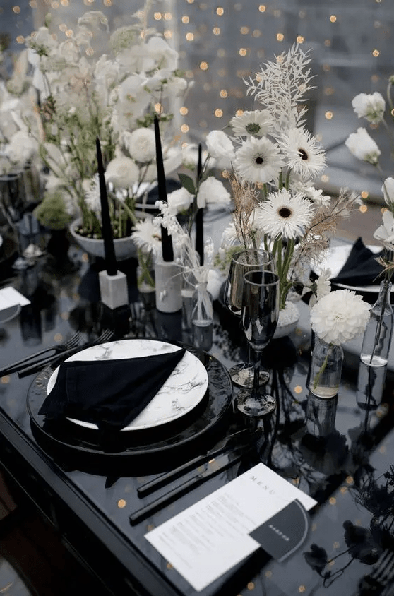 a modern cluster wedding centerpiece of lots of white blooms and leaves in various vases, tall and thin black candles in neutral candleholders