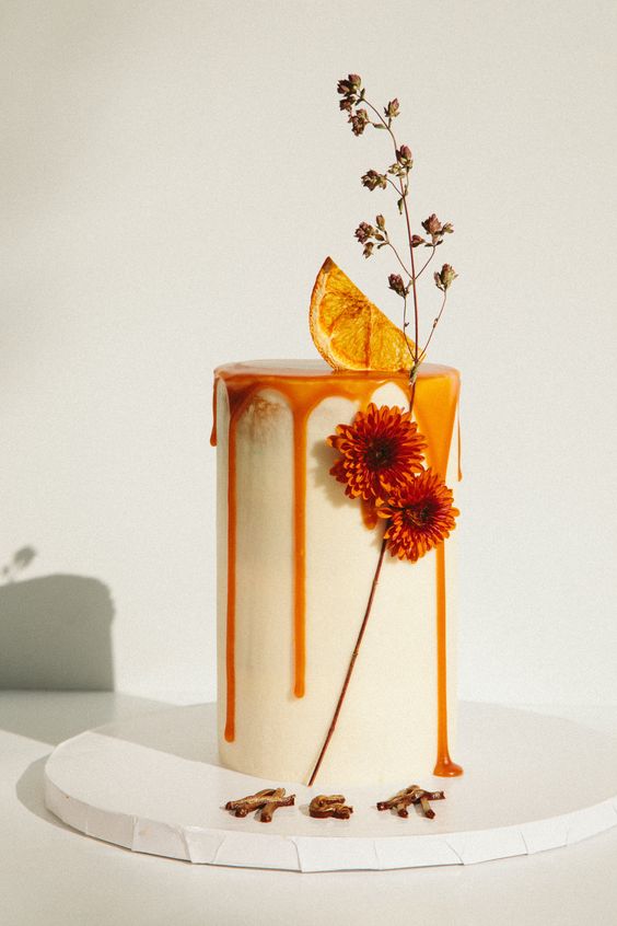 a modern tall wedding cake with caramel drip, a citrus slice, orange blooms and dried ones for a fall wedding