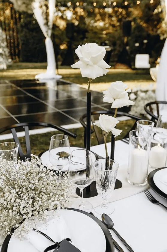 a modern wedding centerpiece of a black tube vase with white roses, baby's breath and pillar candles is a very beautiful and contrasting idea