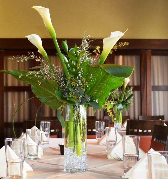 a modern wedding centerpiece of large tropical leaves, callas and some branches is a cool and lovely idea for a modern wedding