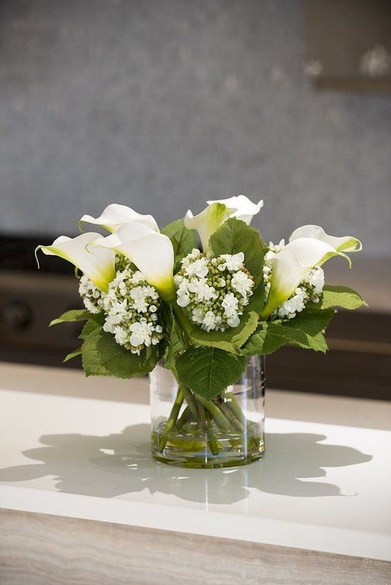 a modern wedding centerpiece of white callas, large leaves and some fillers is a cool idea for a modern wedding