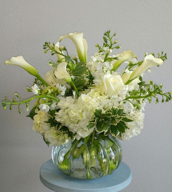 a modern wedding centerpiece of white roses, hydrangeas and callas plus foliage is a cool and catchy idea