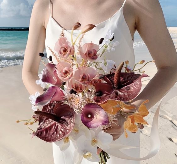 a moody fall wedding bouquet of purple anthuriums, pink and orange orchids, some fillers is a cool idea