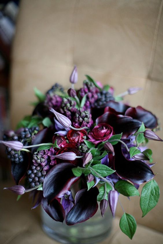 a moody wedding centerpiece of burgundy ranunculus, deep purple callas and berries plus foliage for a moody fall wedding