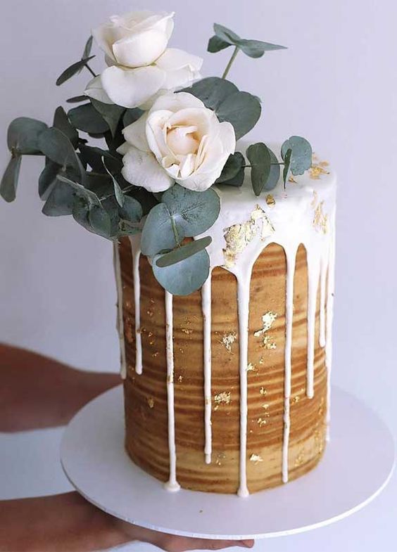 a naked tall wedding cake with creamy drip and gold leaf, white roses and eucalyptus on top is adorable for spring