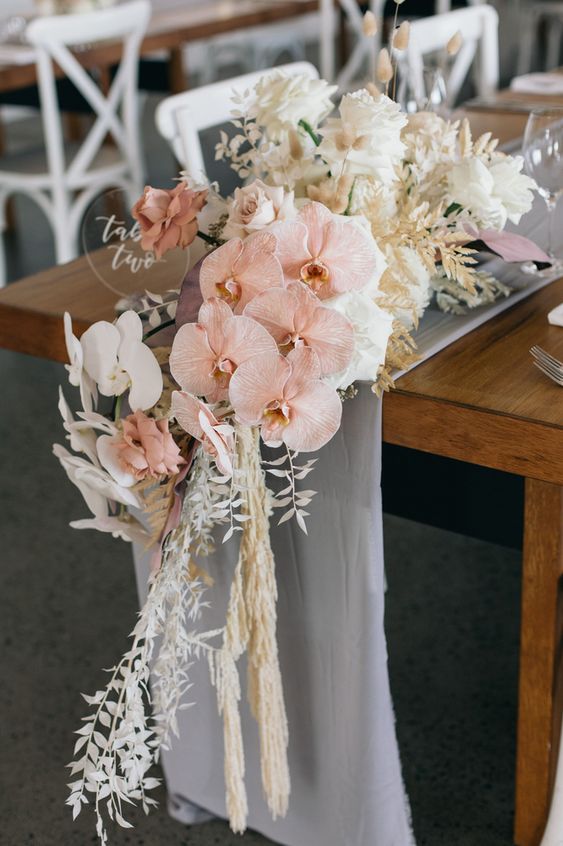 a neutral cascading wedding centerpiece of white roses, pink and white orchids, grasses and leaves and some bunny tails