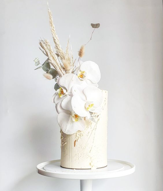 a neutral tlal wedding cake with white orchids, pampas grass and other grasses is a gorgeous idea