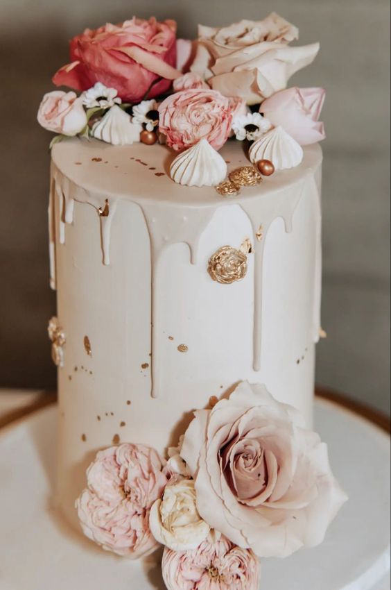 a neutral wedding cake with matching drip and gold touches, meringues, pink blooms and beads on top is a chic and refined idea