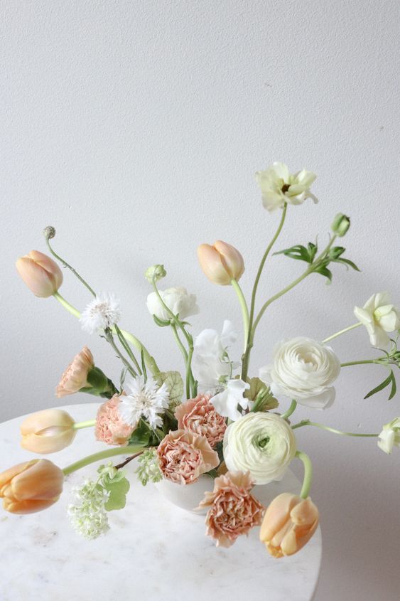 a neutral wedding centerpiece of peachy tulips and carnations and white ranunculus is amazing for a modern wedding
