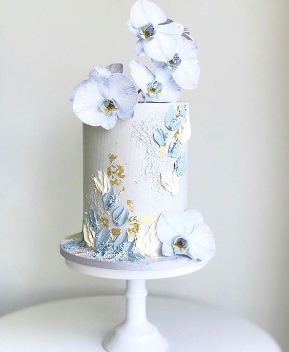 a pastel blue tall wedding cake with painted blue and yellow blooms, gold leaf and pastel blue orchids for a spring wedding