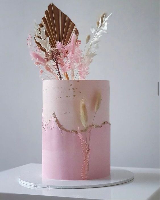 a pink and blush wedding cake with a gold touch, a frond and dried leaves for a spring or summer wedidng
