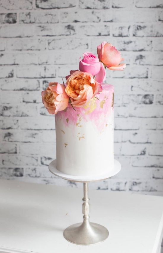 a pink and white watercolor wedding cake with gold leaf and pink and peachy blooms on top for spring or summer