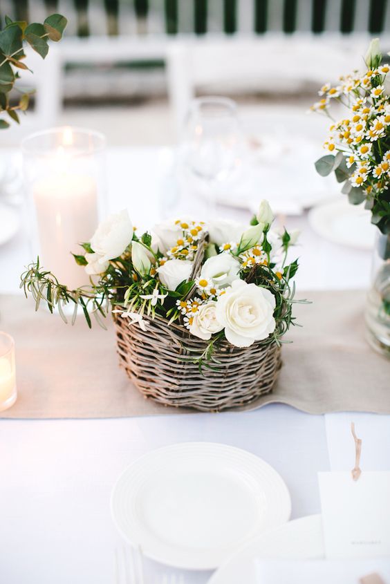 a pretty rustic wedding centerpiece of a basket with white roses, chamomiles and some greenery is a gorgeous idea for a summer wedding
