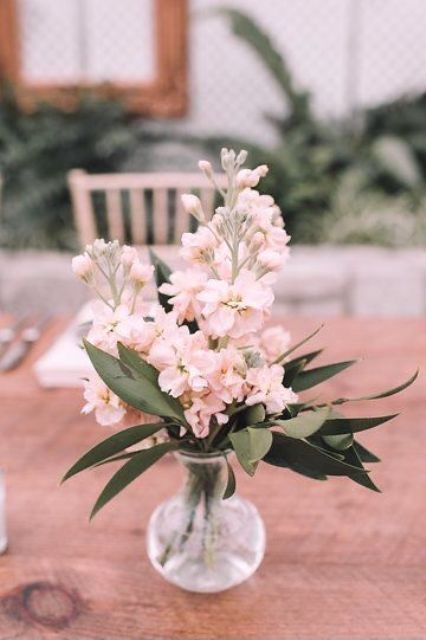 a pretty wedding centerpiece of pink blooms and greenery placed in a clear vase is all you need for a casual wedding