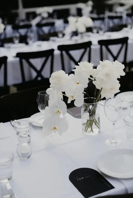 a refined modern wedding tablescape with a white tablecloth, grey and black menus, a white rose and orchid centerpiece is chic