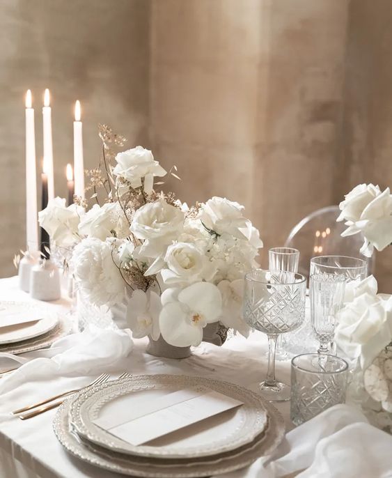 a refined white wedding centepiece of roses, orchids and some dried grasses for a touch of texture