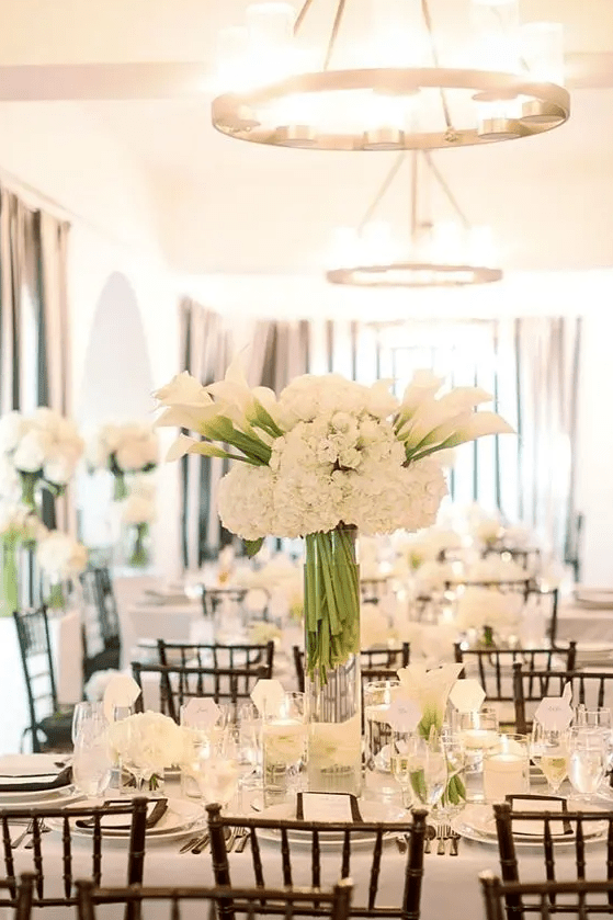 a refined white wedding centerpiece of hydrangeas and callas surrounded with roses and callas on the table