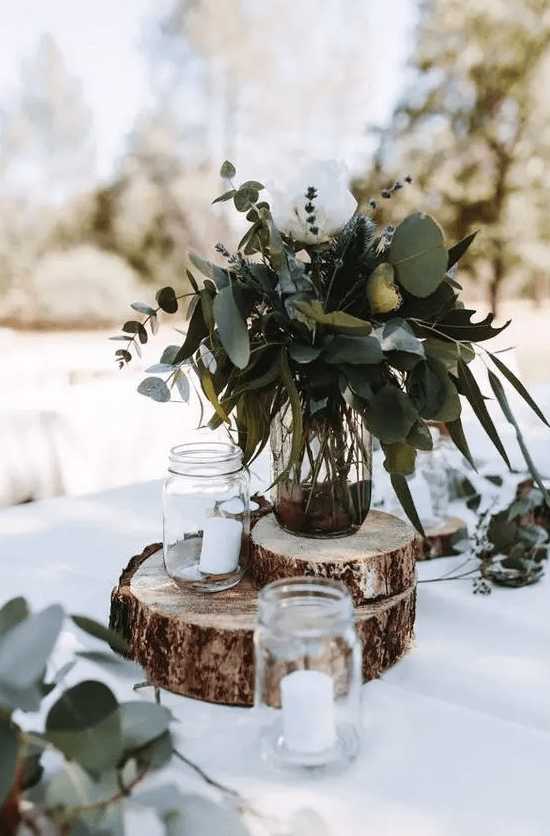 a rustic backyard wedding centerpiece of wood slices, candles, a greenery and lavender arrangement on top