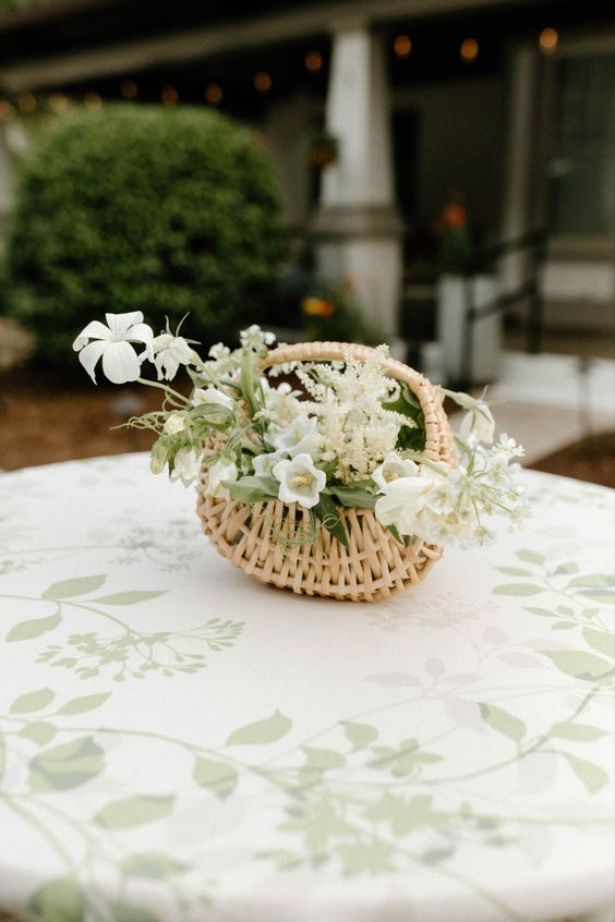 a rustic wedding centerpiece of a basket with white blooms and greenery is a cool idea for a modern rustic wedding