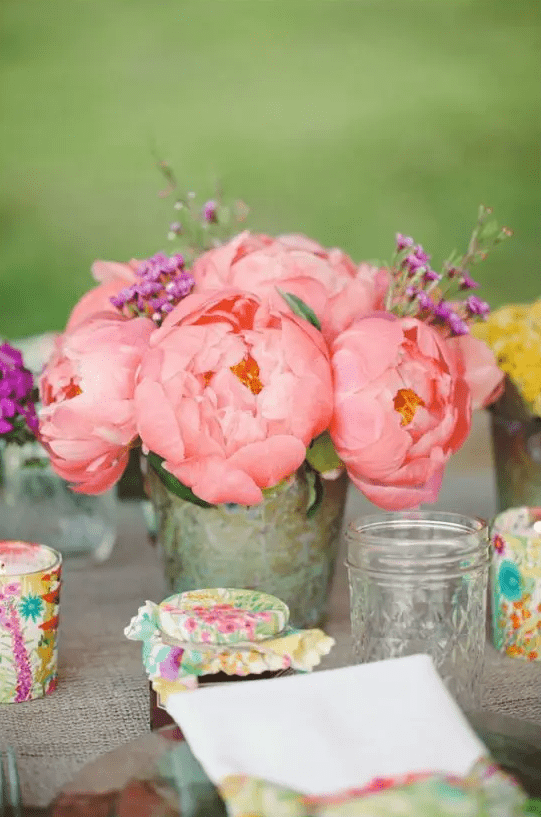 a rustic wedding centerpiece of bold pink peonies and little purple blooms and greenery for a bright summer wedding