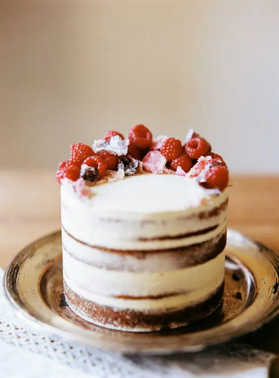 a semi-naked wedding cake with fresh raspberries on top is a cool idea for a summer wedding