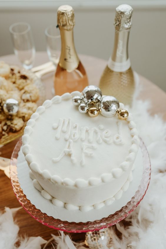 a simple and fun white wedding cake decorated with letters and disco balls is a cool idea for a party-inspired wedding