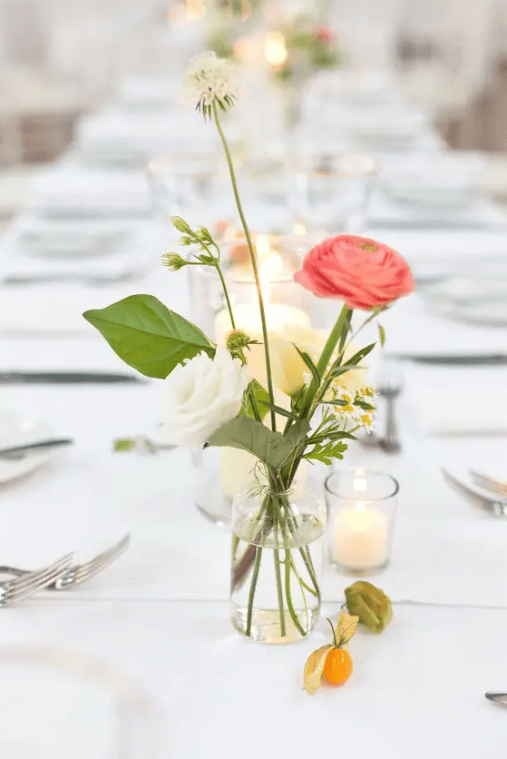 a simple and subtle wedding centerpiece of a white and pink ranunculus, some bouquet fillers and greenery and candles around