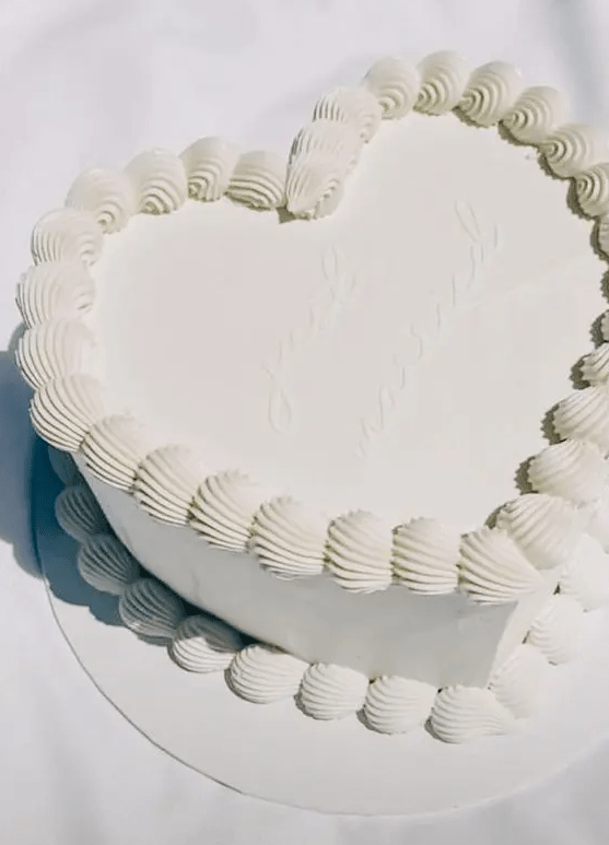 a simple and trendy white heart-shaped wedding cake decorated with sugar details and calligraphy is a pure and clean solution for a modern wedding