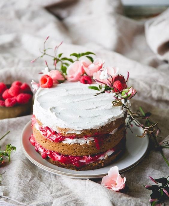 a simple naked wedding cake with frosting, fresh blooms and berries is a delicious dessert for the summer