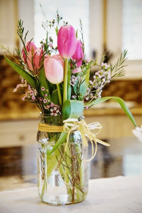 a simple rustic wedding centerpiece of hot pink and light pink tulips, waxflower and greenery in a jar is a gorgeous idea for a wedding with touches of pink