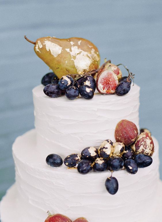 a simple white textural wedding cake topped with gilded grapes, figs and pears is a cool idea for a refined fall wedding